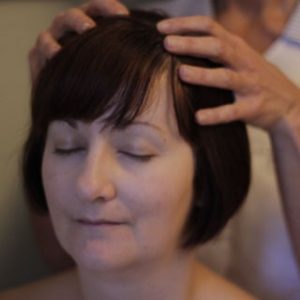 Women with eyes shuts and therapist placing hands on her head